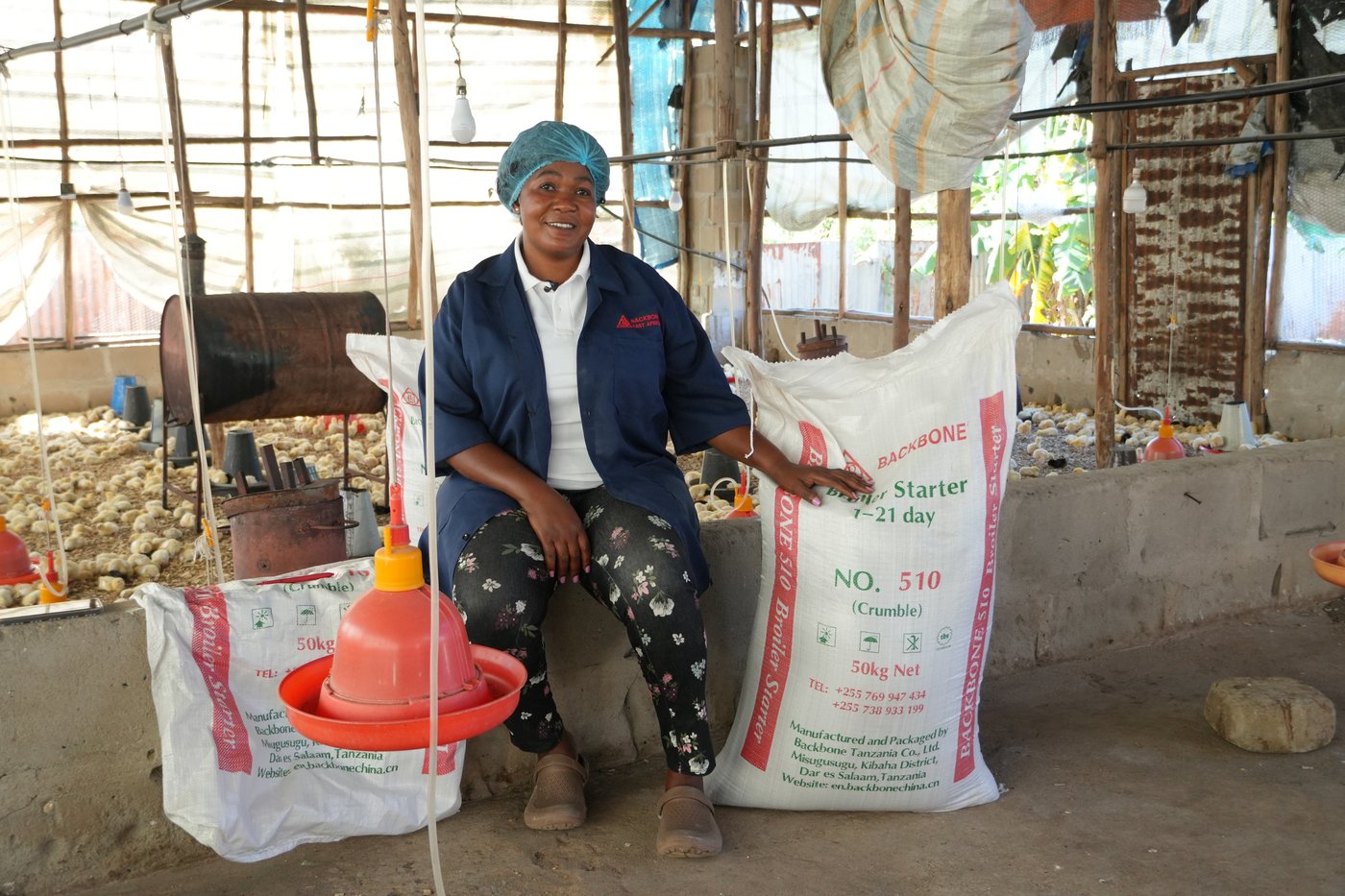 The farmer inside the poultry house, seated beside bags of Backbone-branded Broiler Starter Feed.